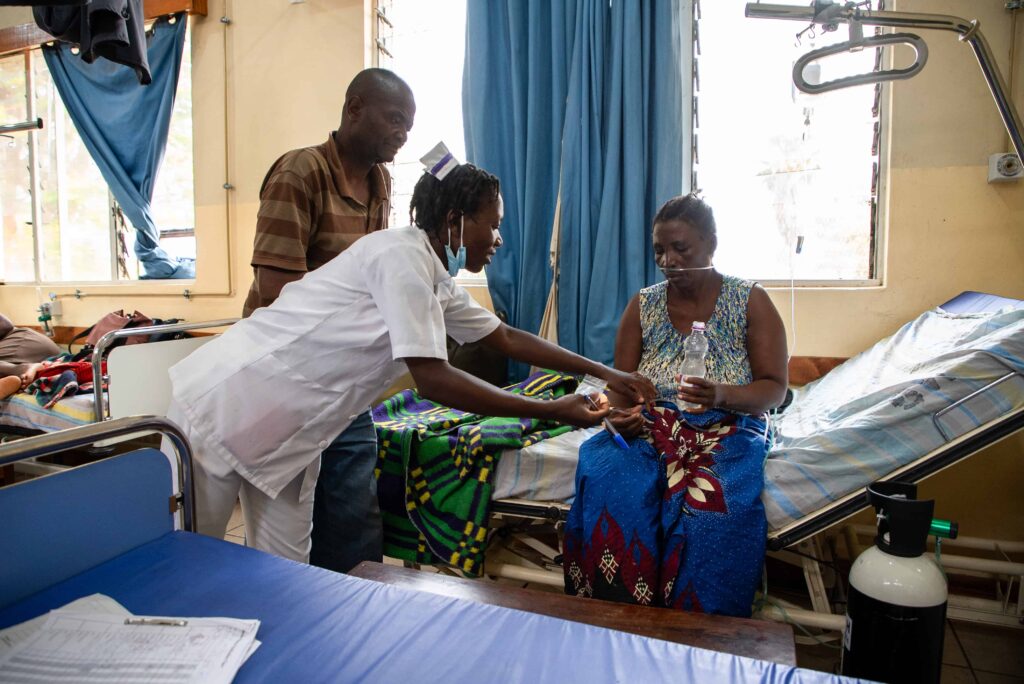 A patient sit in the bed receiving medicine from a nurse