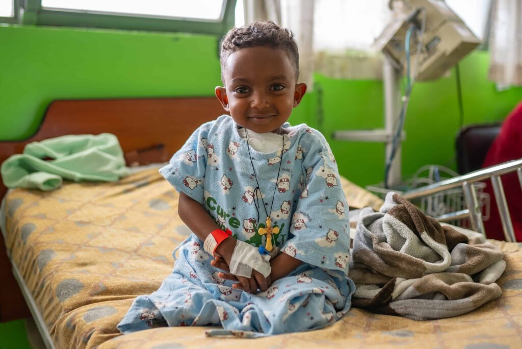 a little boy in a hospital gown, sitting and smiling