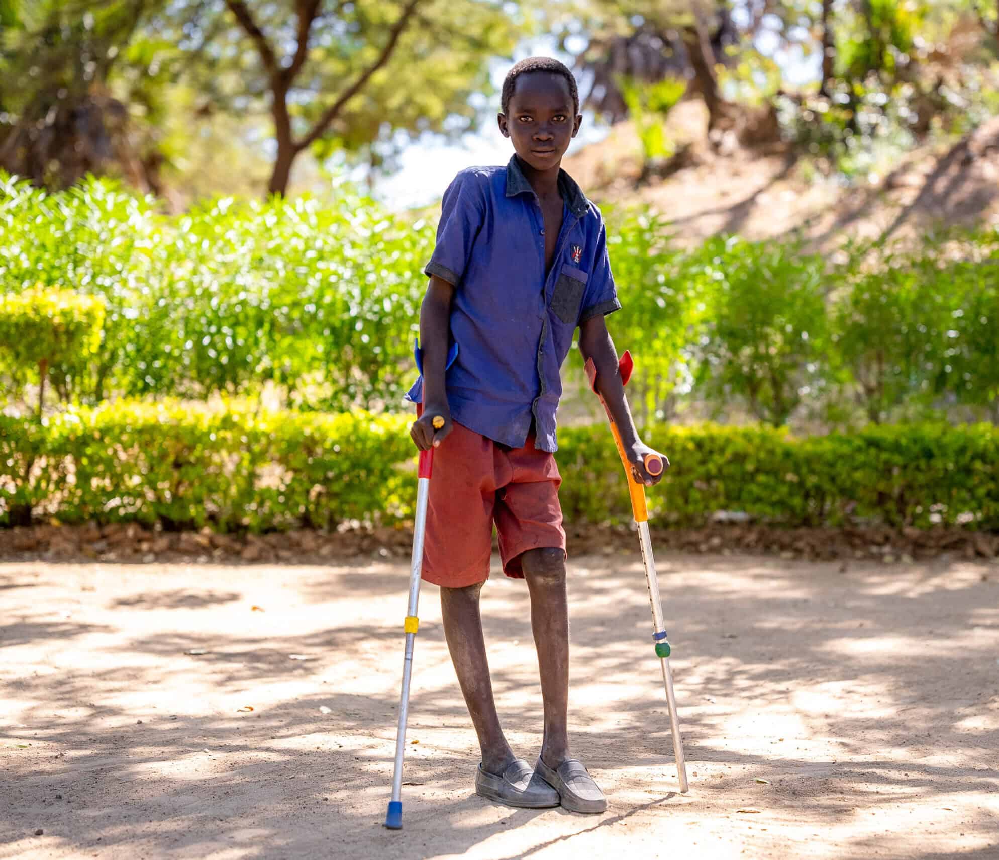 A boy stands outside with two walking sticks