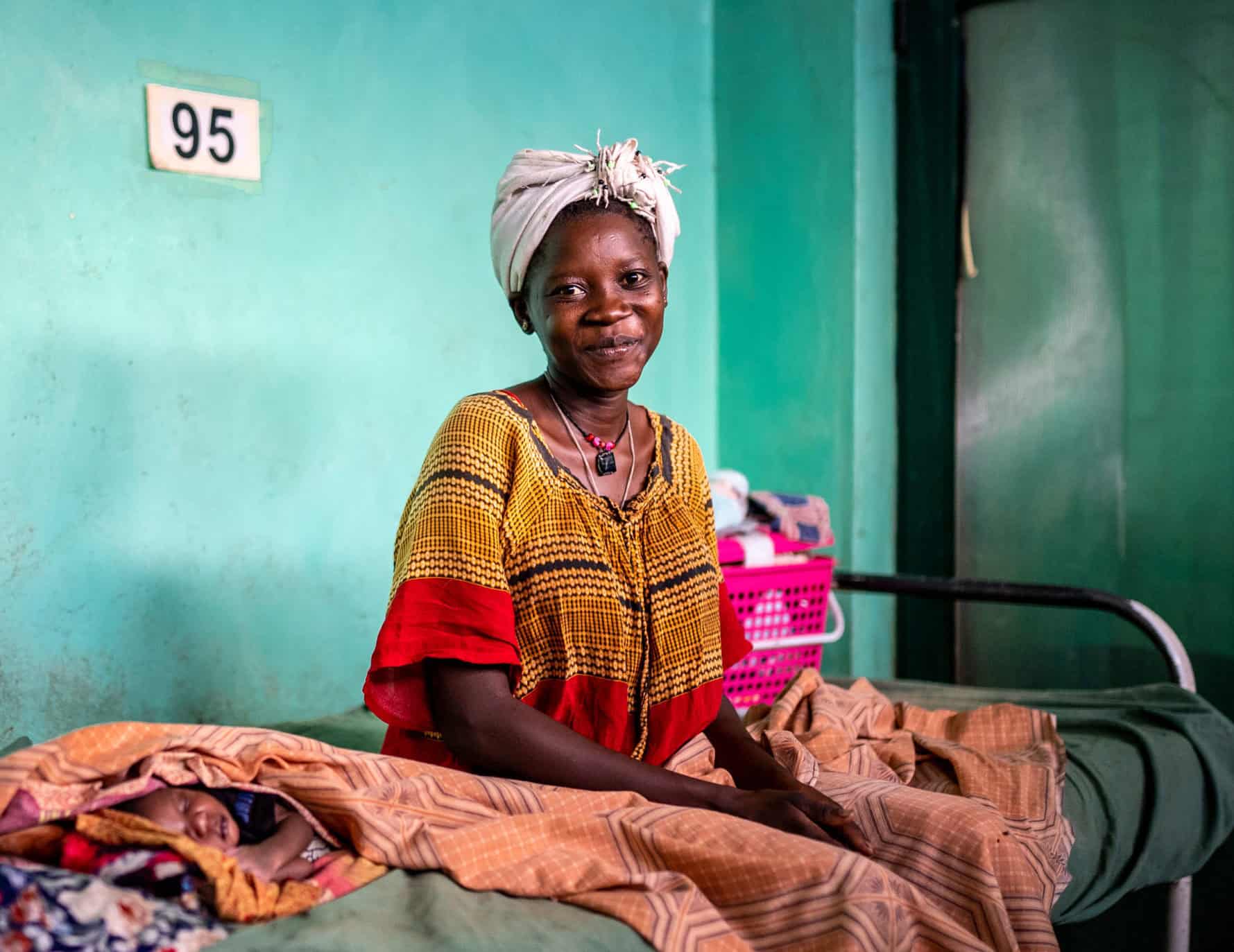 A young smiling woman sits on a hospital bed