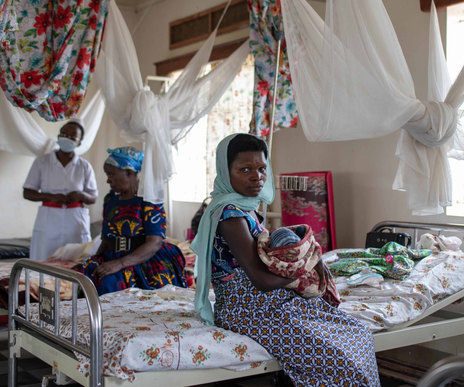 A young African woman sits on a hospital bed