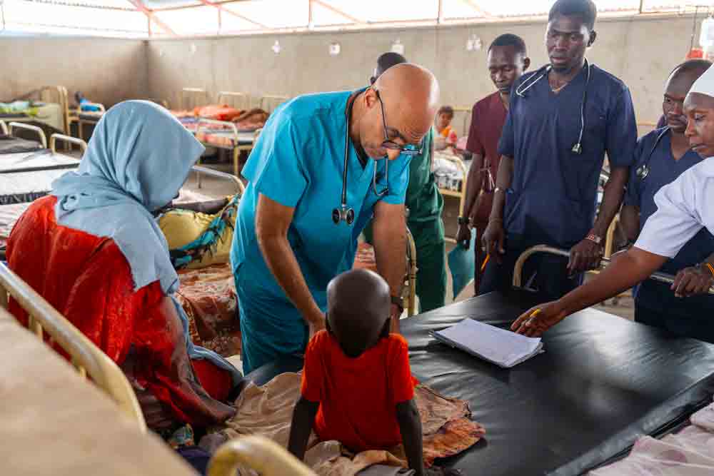 Hospital staff gather around a child and family during rounds in a hospital ward.