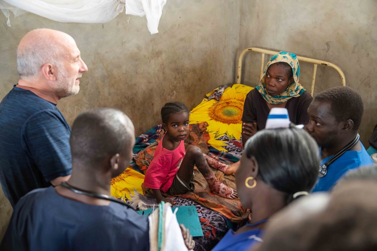 Hospital team assesses a burned child in a hospital room in Sudan while family members watch.