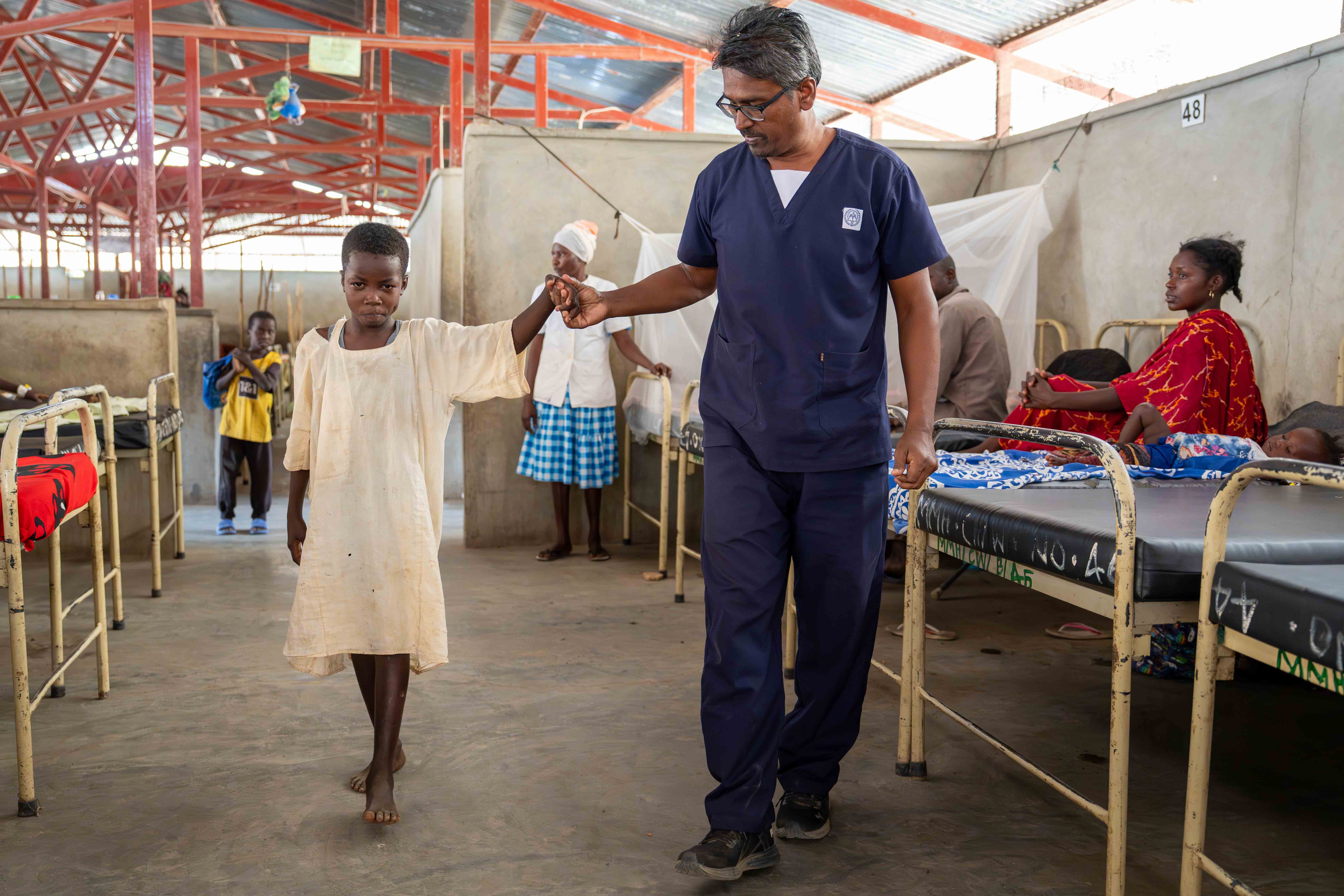 A clinician helps a child walk through a hospital ward during rehabilitation after burn injuries.