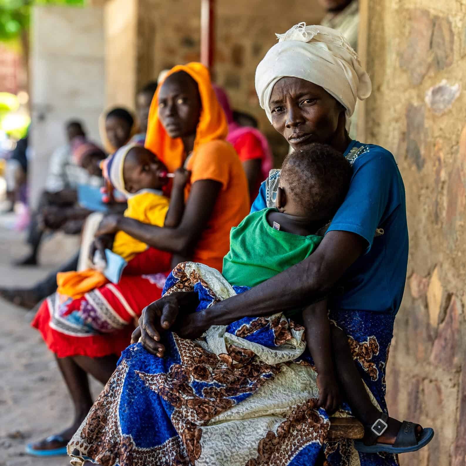 A group of women sit along a wall with their babies